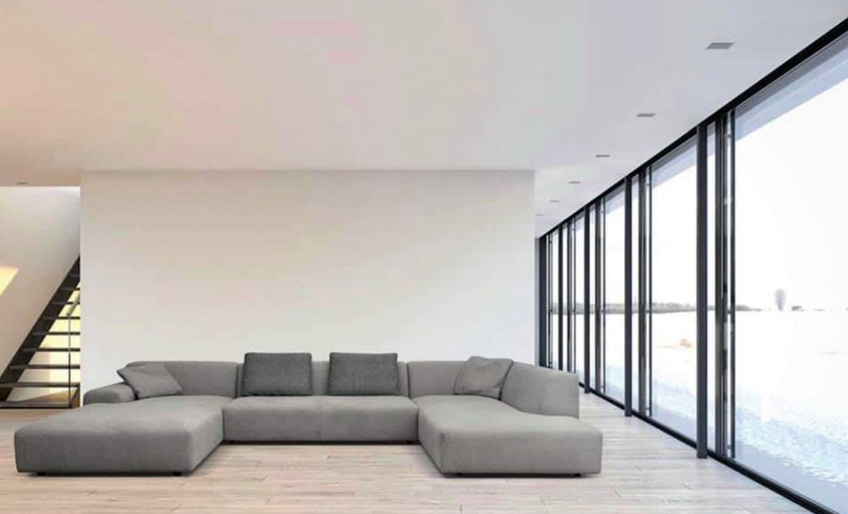 Canapé en U Slow en tissu gris, assise basse et profonde, dans un séjour aux grandes baies vitrées